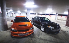 Оранжевый Mitsubishi Lancer и черная Subaru Impreza на парковке